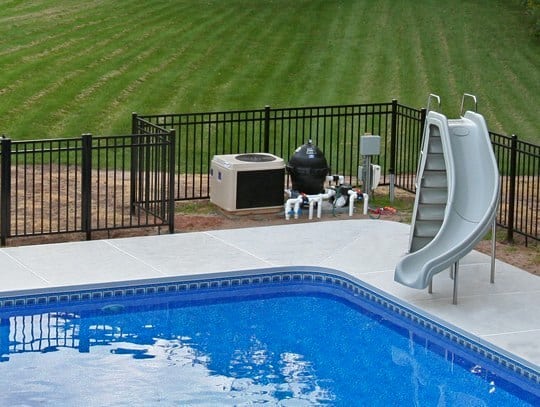 This Is A Photo Of A Lazy L Style Custom Inground Swimming Pool With A Black Fence And Water Slide.