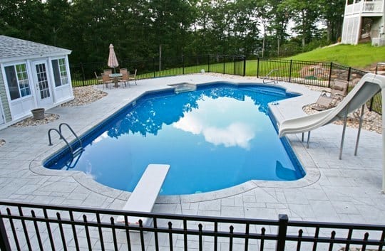 This Is A Photo Of A Lazy L Style Custom Inground Swimming Pool With A Custom Pool House, Water Slide. And Diving Board.