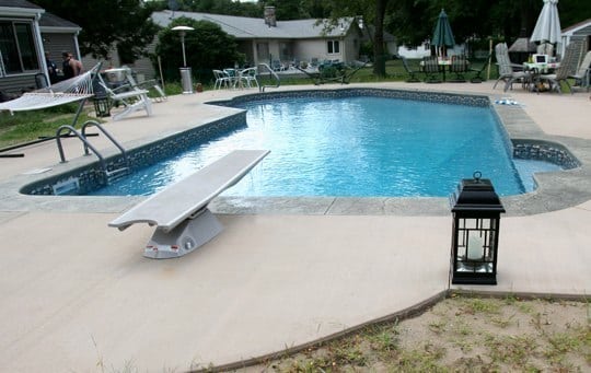 This Is A Photo Of A Lazy L Style Custom Inground Swimming Pool With A Black Steps And Diving Board.