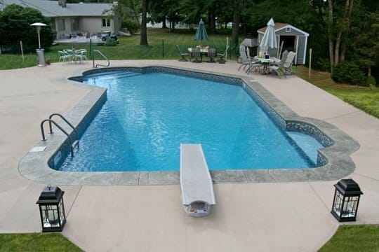 This Is A Photo Of A Lazy L Style Custom Inground Swimming Pool With A Black Fence, Steps And Diving Board.
