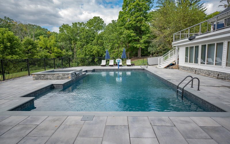 Custom Inground Pool Featuring Patio Lounge Chairs, Stone Hot Tub And Gray Cement Patio