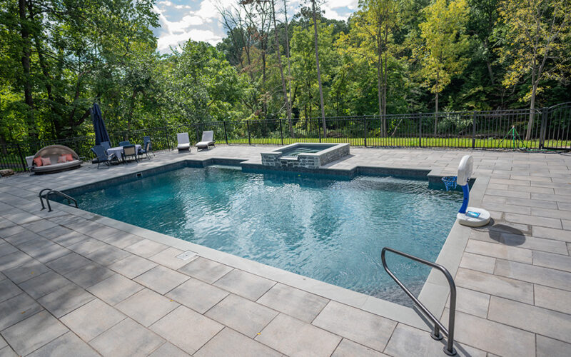 Custom Inground Pool Featuring Patio Furniture, Stone Hot Tub And Gray Cement Patio